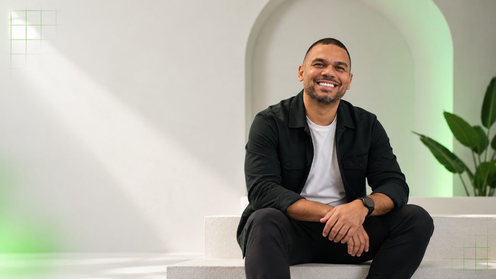 Rafael Soares sorrindo, sentado em uma escada branca com detalhes verdes